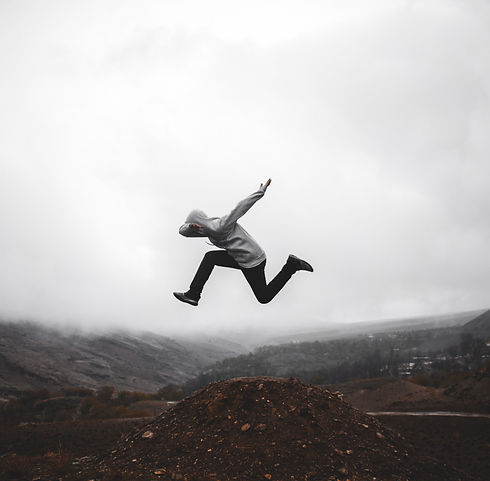 Mountain landscape covered in fog with person in hooded sweatershirt leaping in place in dramatic pose.