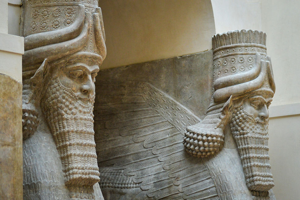Two stone winged human-headed bull statues with intricate beards and headpieces, set against a plain museum wall, conveying grandeur.