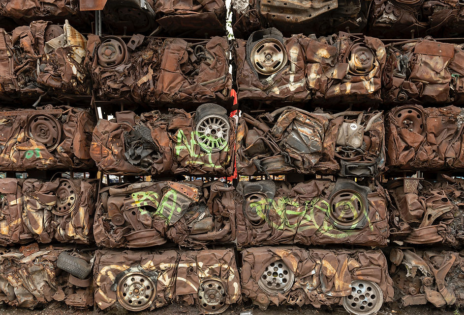 A stacked, crushed, rusty car body with exposed wheels in a space