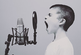 Black and white photo of a young boy with his mouth open wide speaking or shouting into a microphone