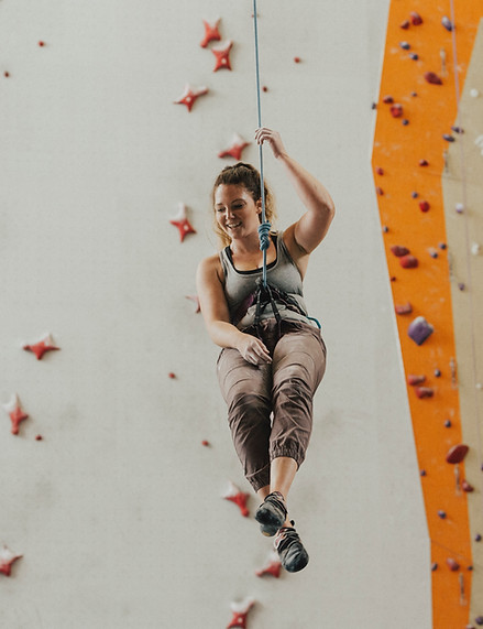 Woman climbing in an indoor wall smiles, hanging on rope.