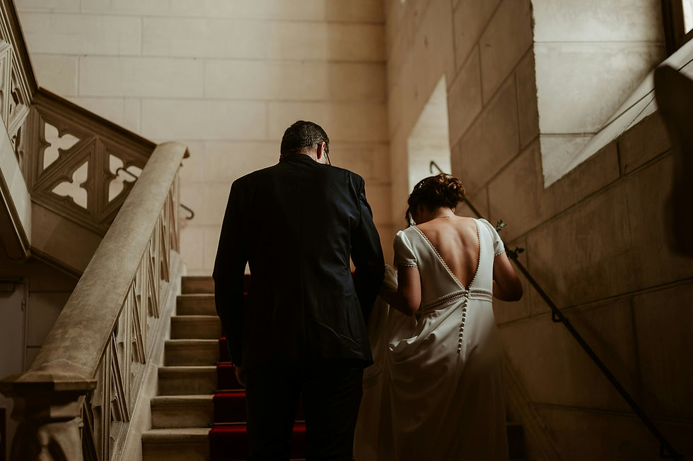 A bride and groom gracefully ascend a grand staircase, the soft lighting and elegant architecture creating a timeless and romantic scene.