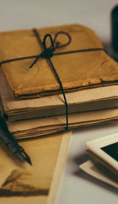 An aged bundle of letters and photos with a pot of ink and ink pen.