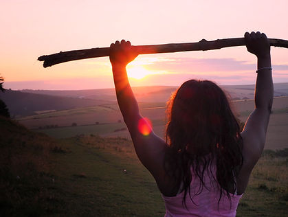 woman holding a walking stick above her head at the top of a mountain celebrating success