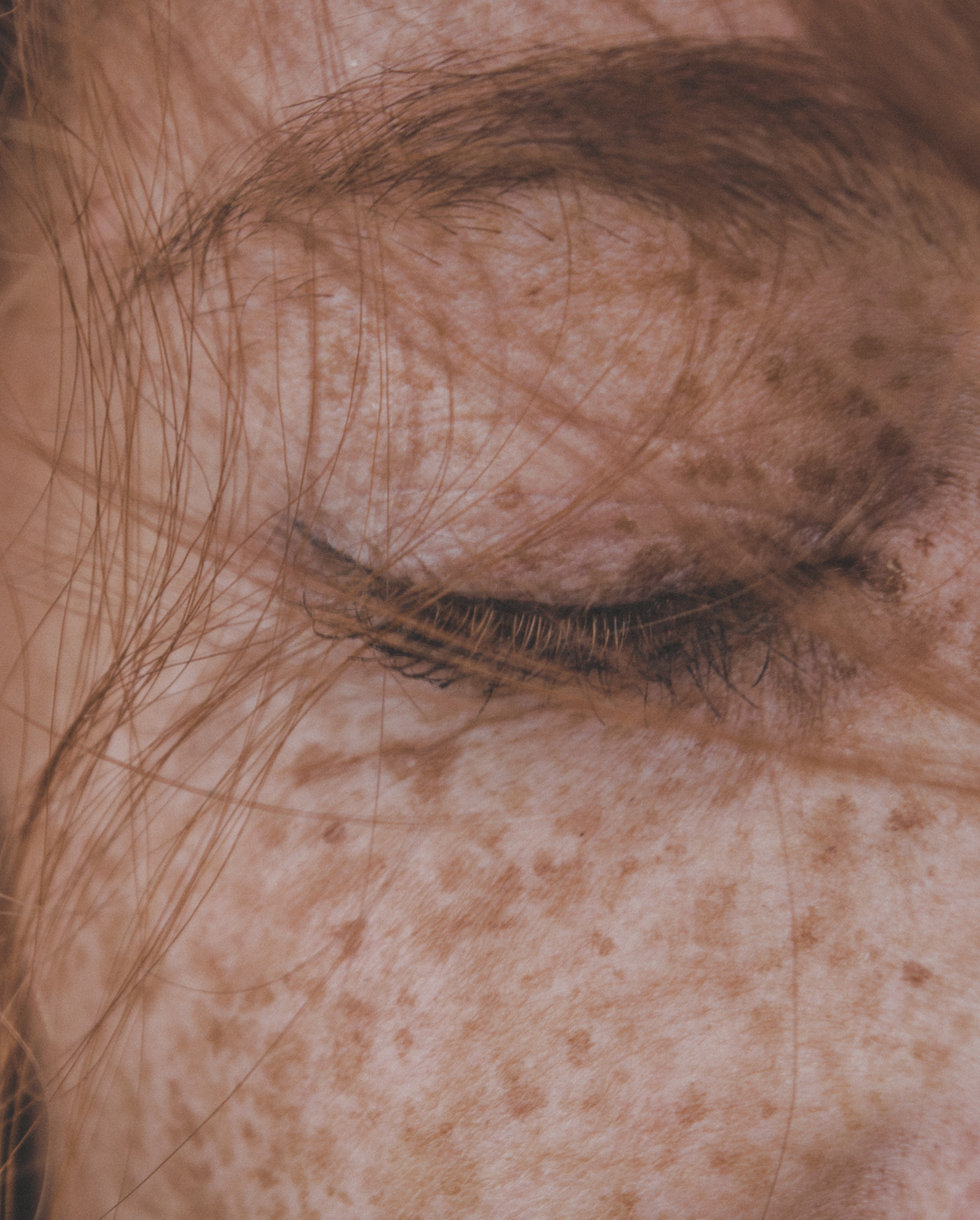 Close-up of a freckled face with eyes closed and hair blowing