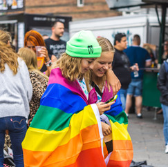Two feminine youth holding each other with a pride flag wrapped around them.