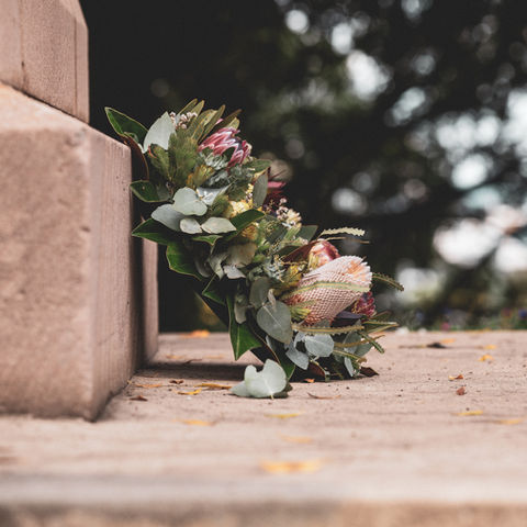 Floral bouquet with green leaves rests on a stone ledge outdoors, with soft blurred trees in the background.
