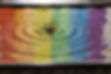 Water dropping into a pool of water, creating ripples, with a reflection of a rainbow