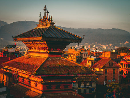 Sunset illuminates the intricate architecture of traditional buildings in Kathmandu, with distant hills creating a serene backdrop.