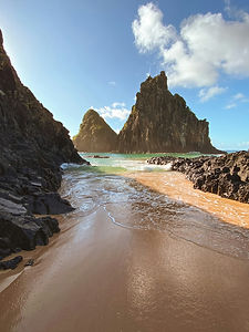 Two rocky peaks rise from turquoise water behind a narrow beach at Fernando de Noronha