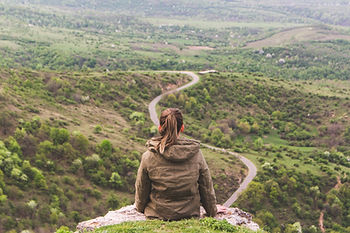 A woman sitting on a rock overlooking a valley with a winding road