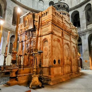 Ornate altar within the Church of the Holy Sepulchre complex. A detailed interior shot focusing on the ornate stone carvings and decorative elements of the Aedicule, illuminated by soft golden light from tall candles.