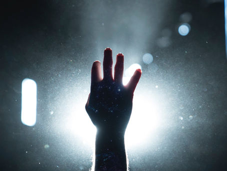 hand reaching toward light in darkness