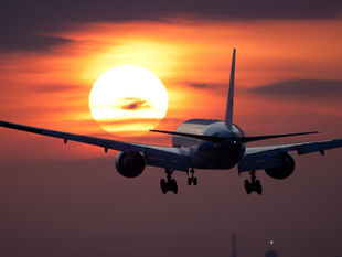 An airliner flying at dusk towards the setting sun.