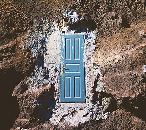 Plano cenital de un terreno rocoso y árido. En medio, rodeado de cal, se encuentra una puerta azul antigua con un picaporte sin llave