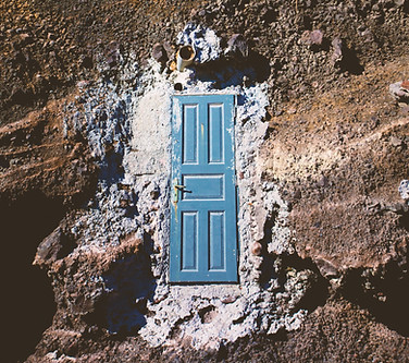 Plano cenital de un terreno rocoso y árido. En medio, rodeado de cal, se encuentra una puerta azul antigua con un picaporte sin llave