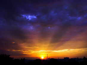 Dramatic sunset over dark city skyline, with glowing orange horizon beneath deep blue and purple storm clouds.