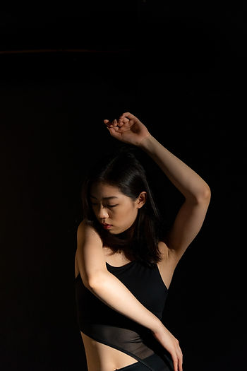 Asiatische Frau mit schwarzen Haaren am Tanzen mit Armen oben und Blick nach unten gerichtet