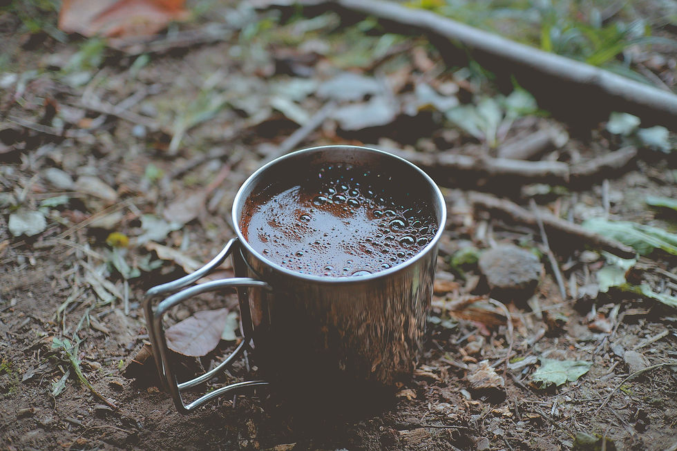 metal cup filled with hot brown liquid on dirt and leaves