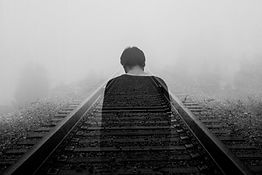 A solitary figure sitting on railway tracks, representing the heavy weight of self-doubt and the challenge of moving forward with confidence.