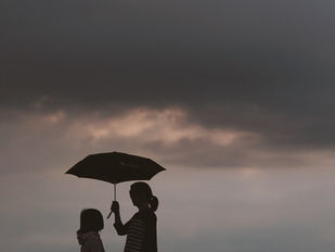 A woman standing next to her daughter holding an umbrella.