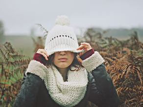 Woman walking alone in the countryside, hat pulled low, with a quietly weary expression.