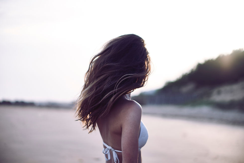 elegant model poses away from camera in bikini top near the ocean photographed by Sean John