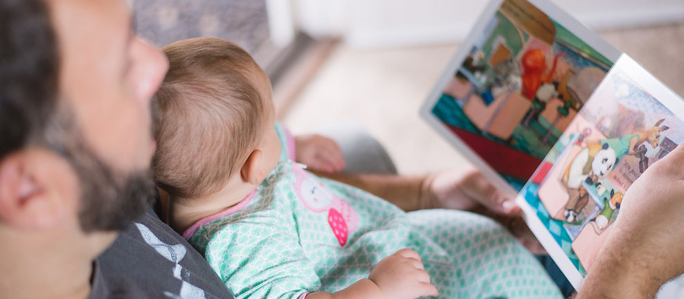 Image of dad reading book to baby in his lap.
