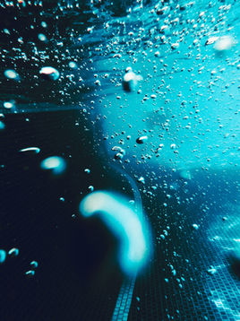 Underwater in a swimming pool, with light and dark blue water and air bubbles swirling around.