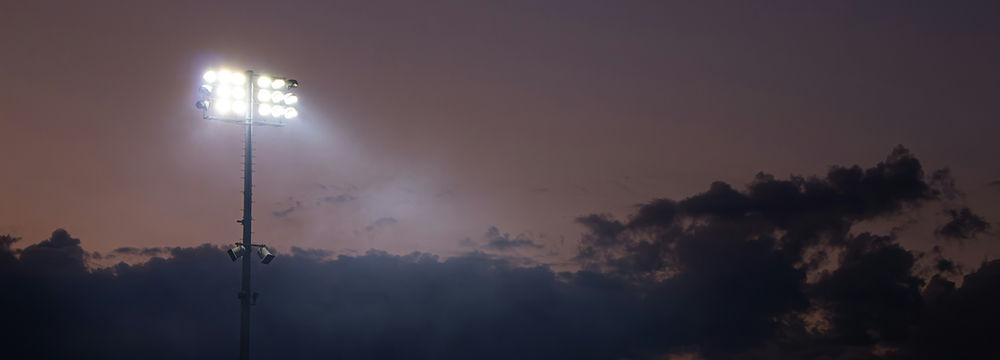 Bright stadium floodlights against a dark evening sky.
