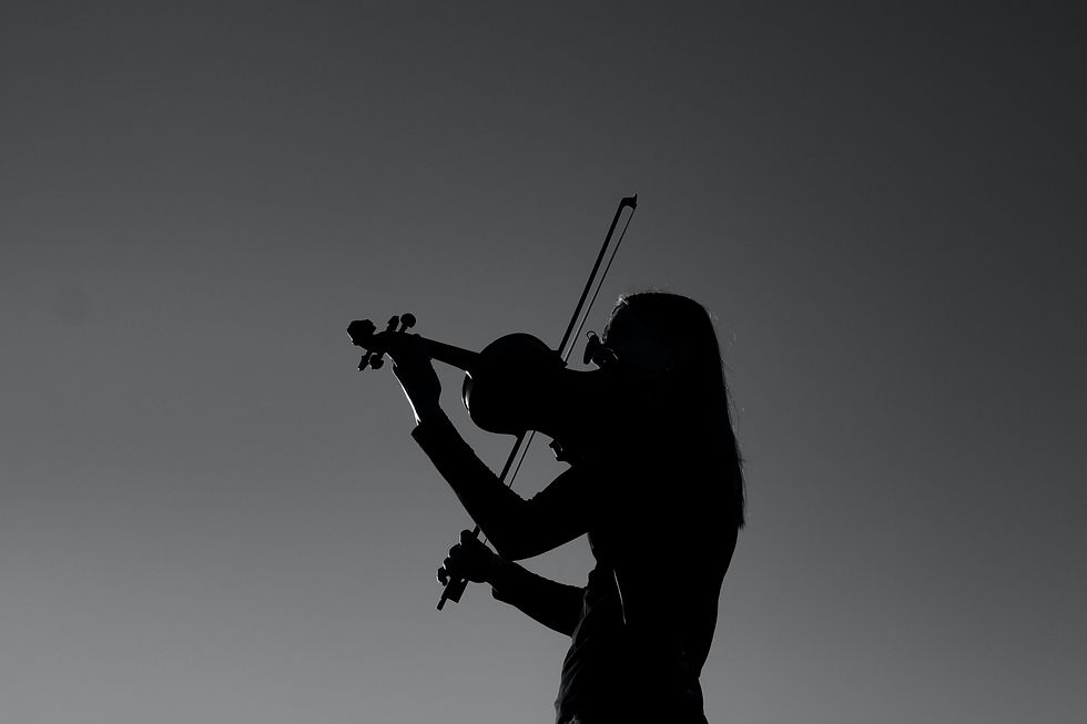 Silhouette of a person playing the violin against a clear, monochromatic sky, evoking a peaceful and contemplative mood.