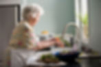 An elderly woman washes vegetables in a kitchen sink. 