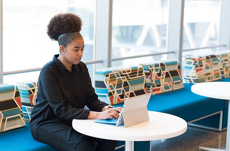 Black professional woman working on a laptop in a modern, brightly lit office lounge — Together We Talent workplace solutions