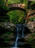 Stone bridge over crisp waterfall flowing over rock formation in Hocking Hills State Park