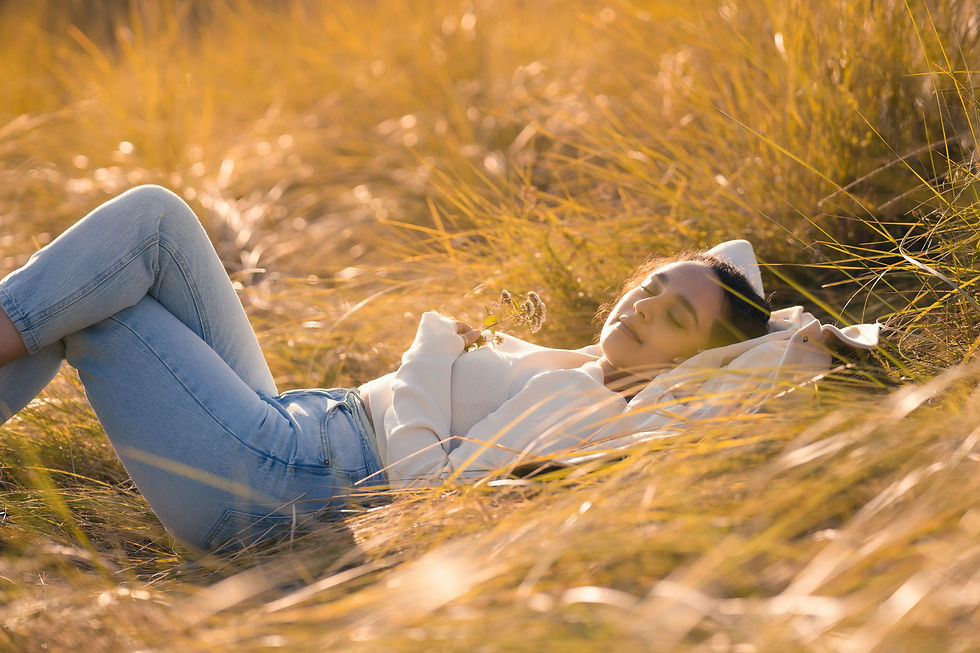 Woman laying back in a field of grass with her eyes shut, soaking in the warm sunlight