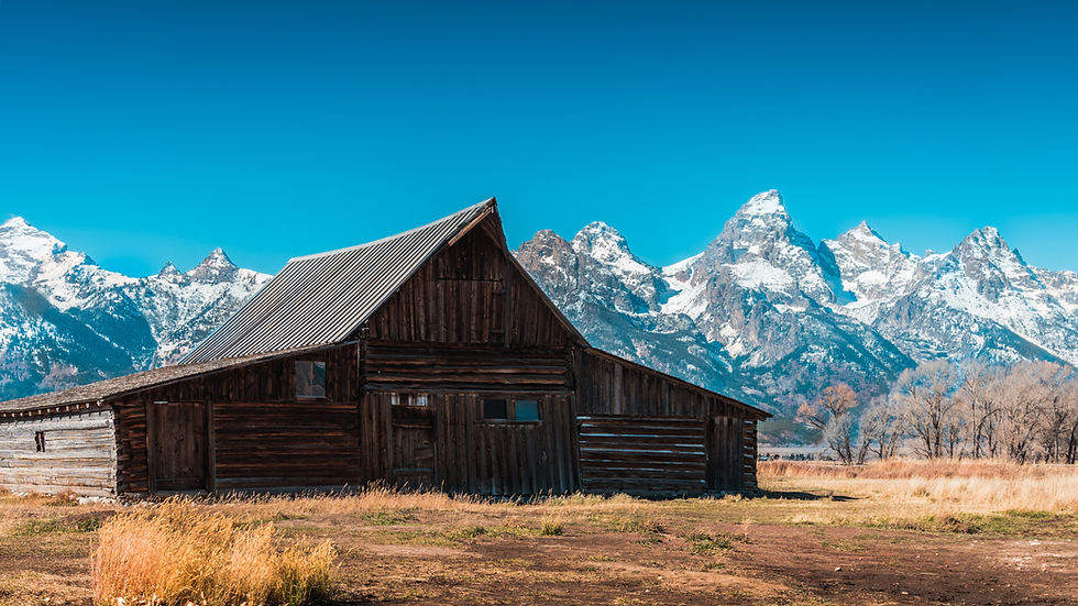 old wooden barn in front of snowy jagged mountain peaks