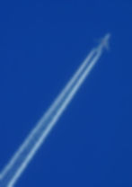 Airplane flying in a clear blue sky, leaving two white contrails. The scene evokes a sense of speed and tranquility.