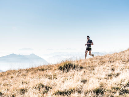 Un homme court sur une colline herbeuse dorée, sous un ciel bleu clair. Montagnes floues en arrière-plan, ambiance paisible.