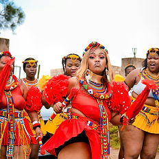 Women in traditional Zulu attire dancing outdoors.