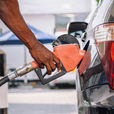 Person fueling a black car at a gas station, close-up of hand holding orange nozzle near rear taillight, calm scene