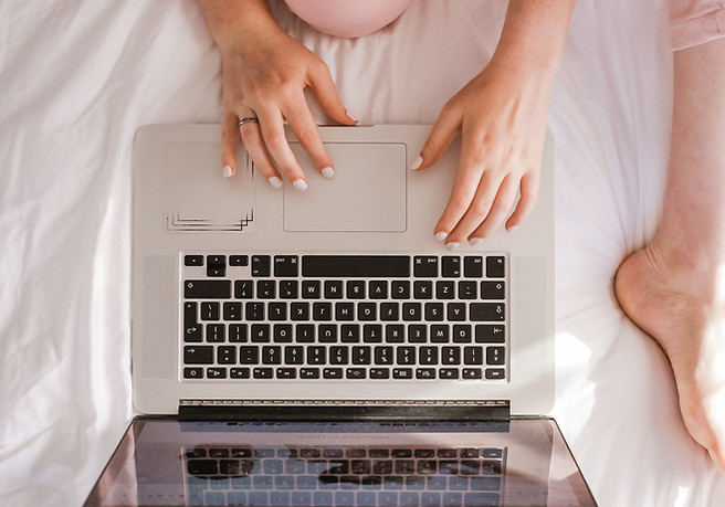 A woman sitting on a bed in front of a laptop by Sincerely Media