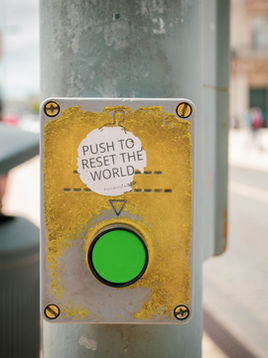 Green button on a city street pole with a worn sticker above it reading “Push to Reset the World".