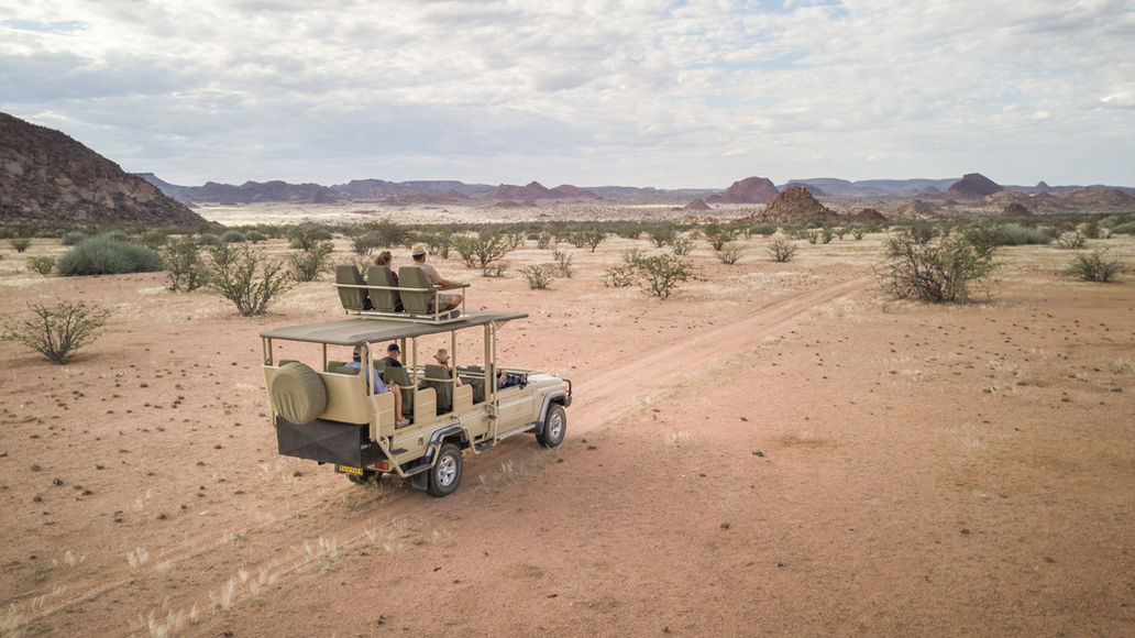 Safari vehicle driving on a dirt road, exploring the African landscape under cloudy skies.
