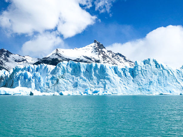 Ghiacciaio patagonico che si affaccia su un lago glaciale con montagne innevate sullo sfondo.