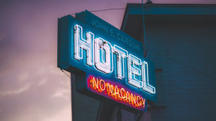 Retro neon sign reading "HOTEL" with a glowing "NO VACANCY" message underneath, set against a dusky sky.