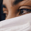 Close up of a woman's sad eyes with a white fabric covering her lower face.