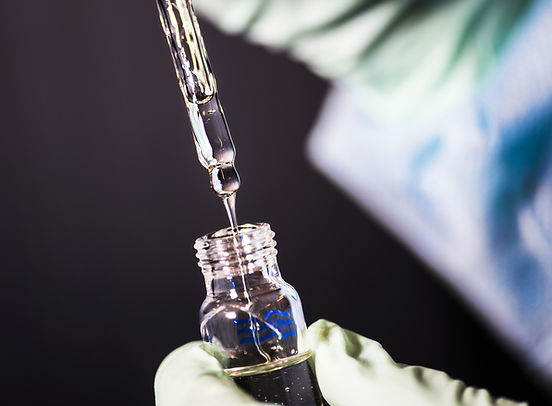 Close-up of a laboratory technician using a glass pipette to transfer a liquid sample into a small vial, wearing protective gloves.