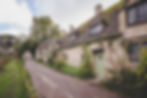 A row of English countryside cottages with sage green front doors and thatched roofs.