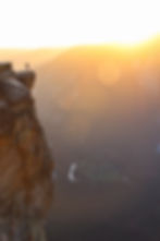 Man standing on a cliff edge with arms outstretched facing the setting sun