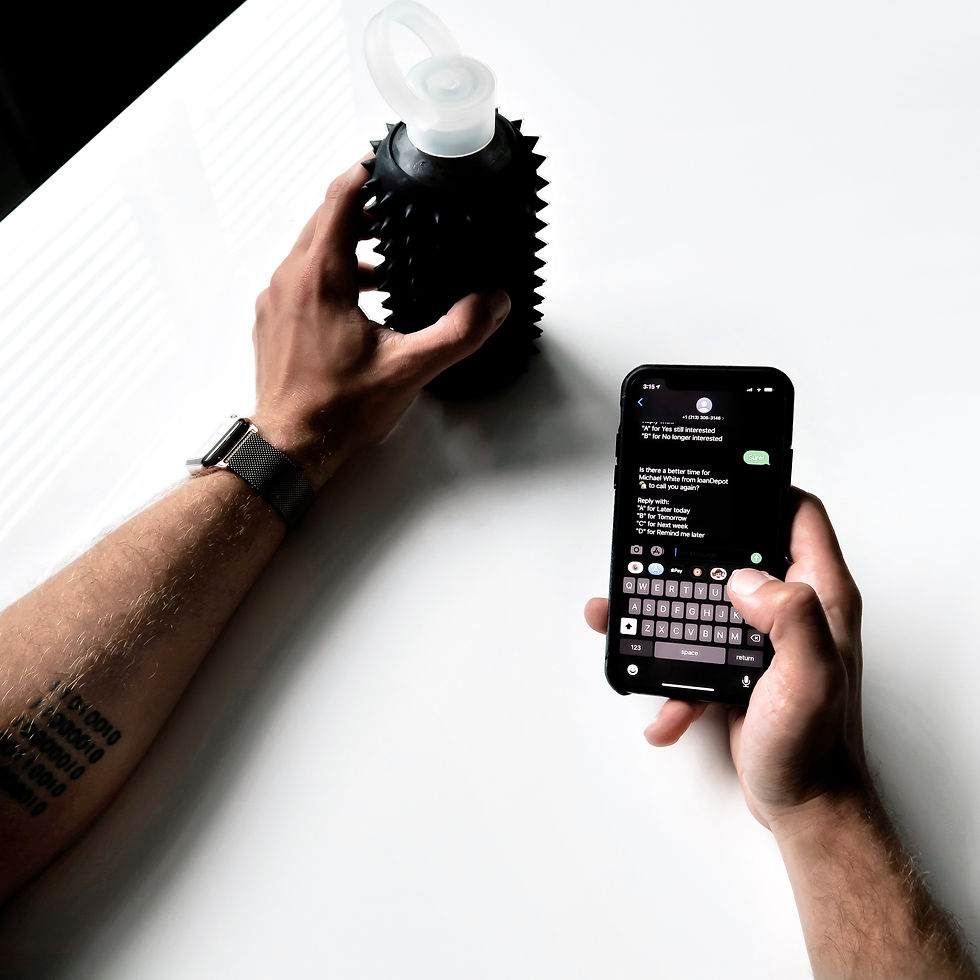 Photo of a person's two arm, one is holding a phone with a smishing text and the other hand is holding a water bottle